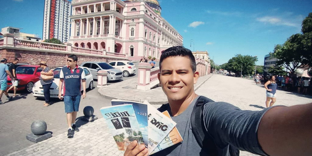 Alex Alves com alguns livros em uma selfie em frente ao TeatroAmazonas